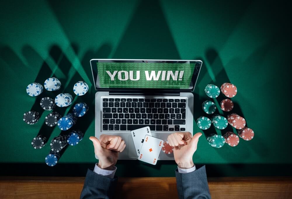 Laptop med orden "You win!", spelmarker, spelkort och två armar med händer som gör tummen upp